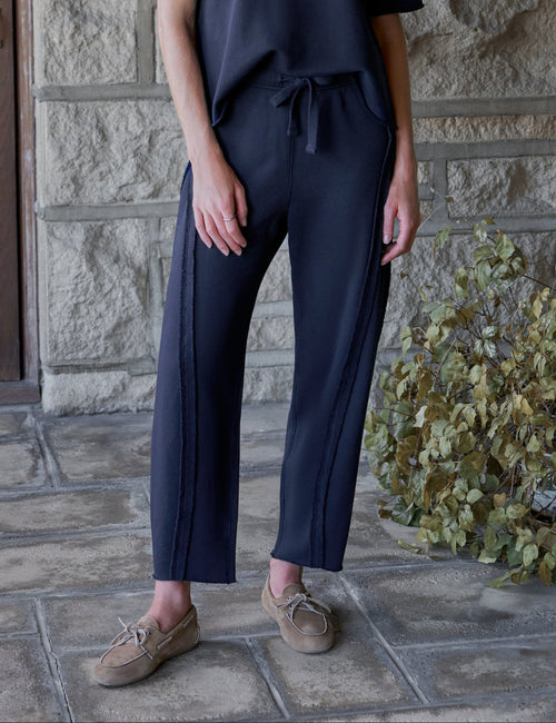 A woman stands on a stone patio wearing a dark navy short-sleeve top and matching navy wide-leg pants with a drawstring waist, paired with tan lace-up shoes., front view