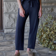 A woman stands on a stone patio wearing a dark navy short-sleeve top and matching navy wide-leg pants with a drawstring waist, paired with tan lace-up shoes.