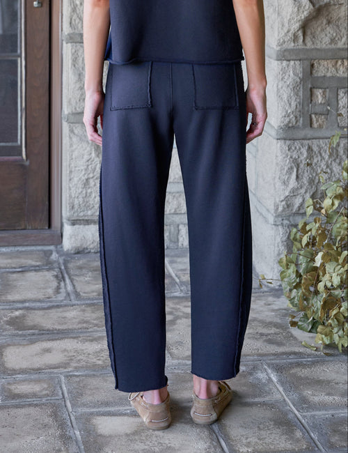 A woman stands on a stone porch wearing a dark navy blue short-sleeve top and matching wide-leg trousers, viewed from the back., alternate view