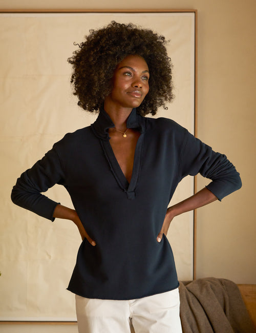 Woman wearing a navy blue long-sleeve top with a beige wall in the background, front view