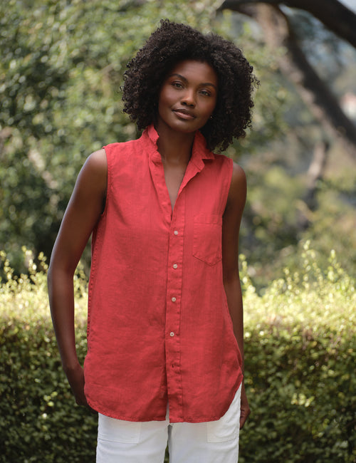 Woman wearing a red sleeveless shirt standing outdoors with greenery in the background, front view