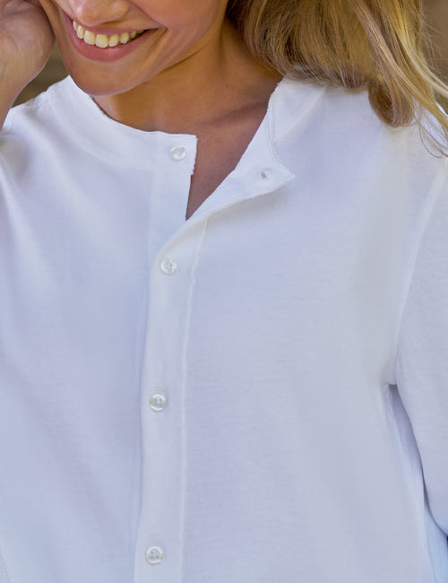 Close-up of a woman wearing a white long-sleeve button-front top with a split neckline and white buttons., view 3