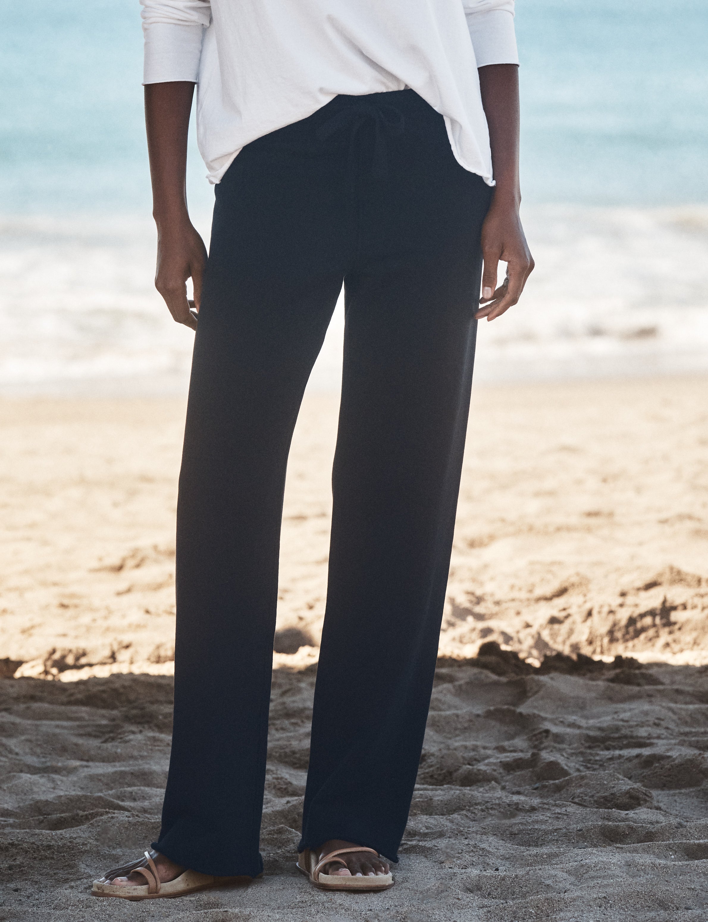 Person wearing navy pants and a white shirt on a beach, front view