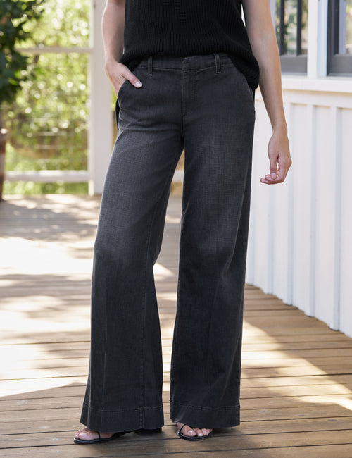Person wearing dark gray wide-leg jeans on a wooden deck., front view