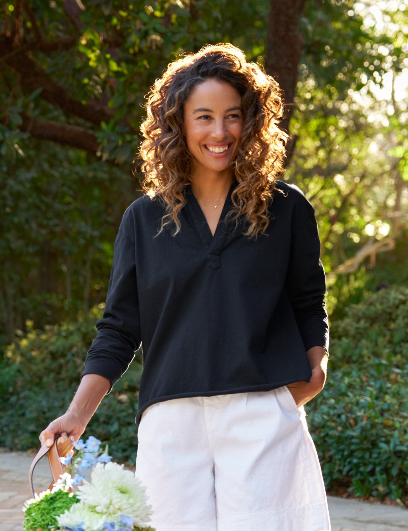 Woman in navy top and white shorts holding flowers by a pool