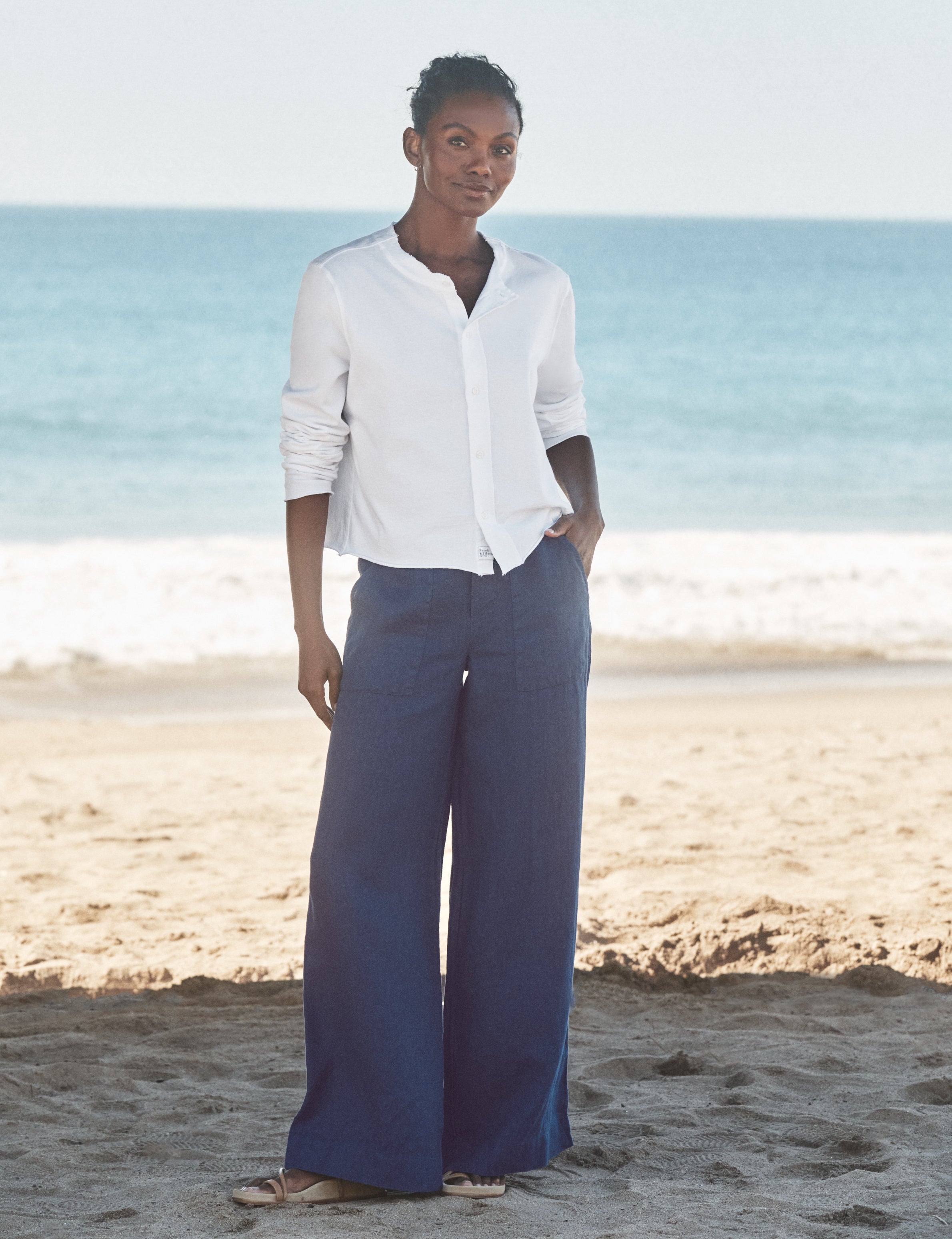 Woman standing on a beach wearing a white shirt and navy pants., view 5