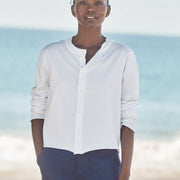 Person wearing a white shirt and dark pants standing on a beach with ocean in the background