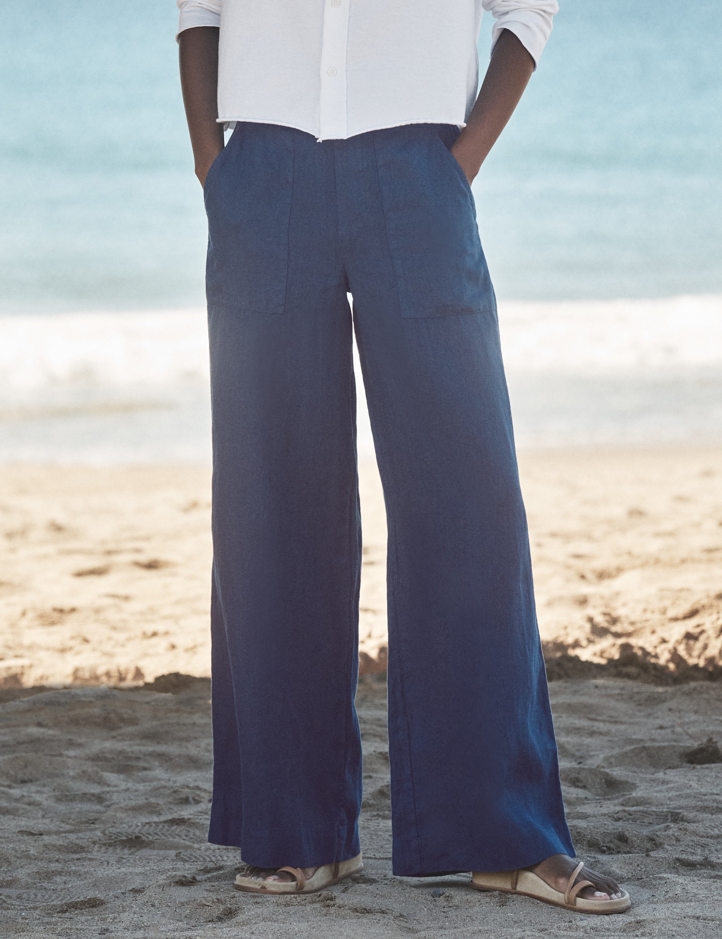 Person wearing blue wide-leg pants and a white shirt on a beach., front view