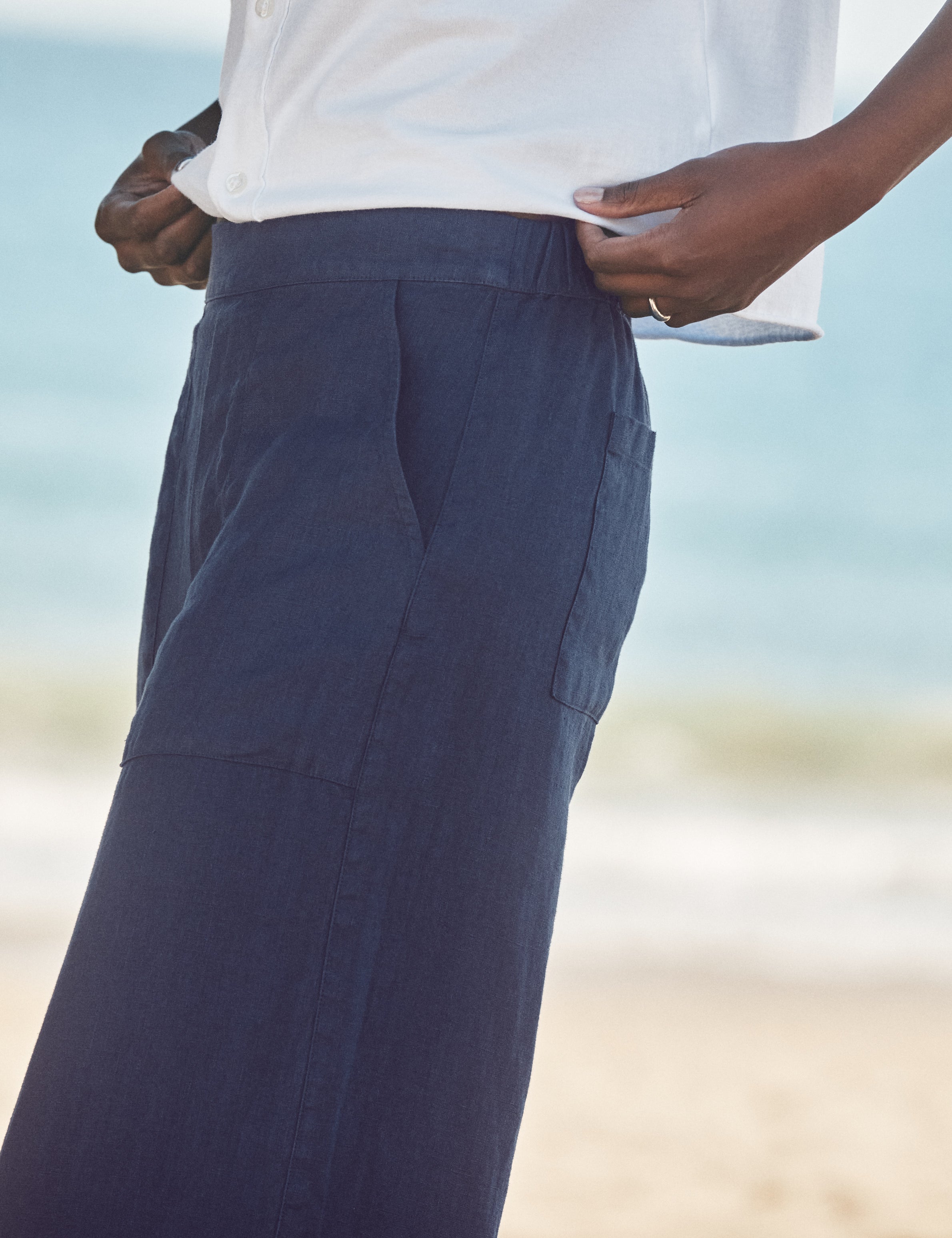 Person wearing navy pants with a blurred beach background, view 3