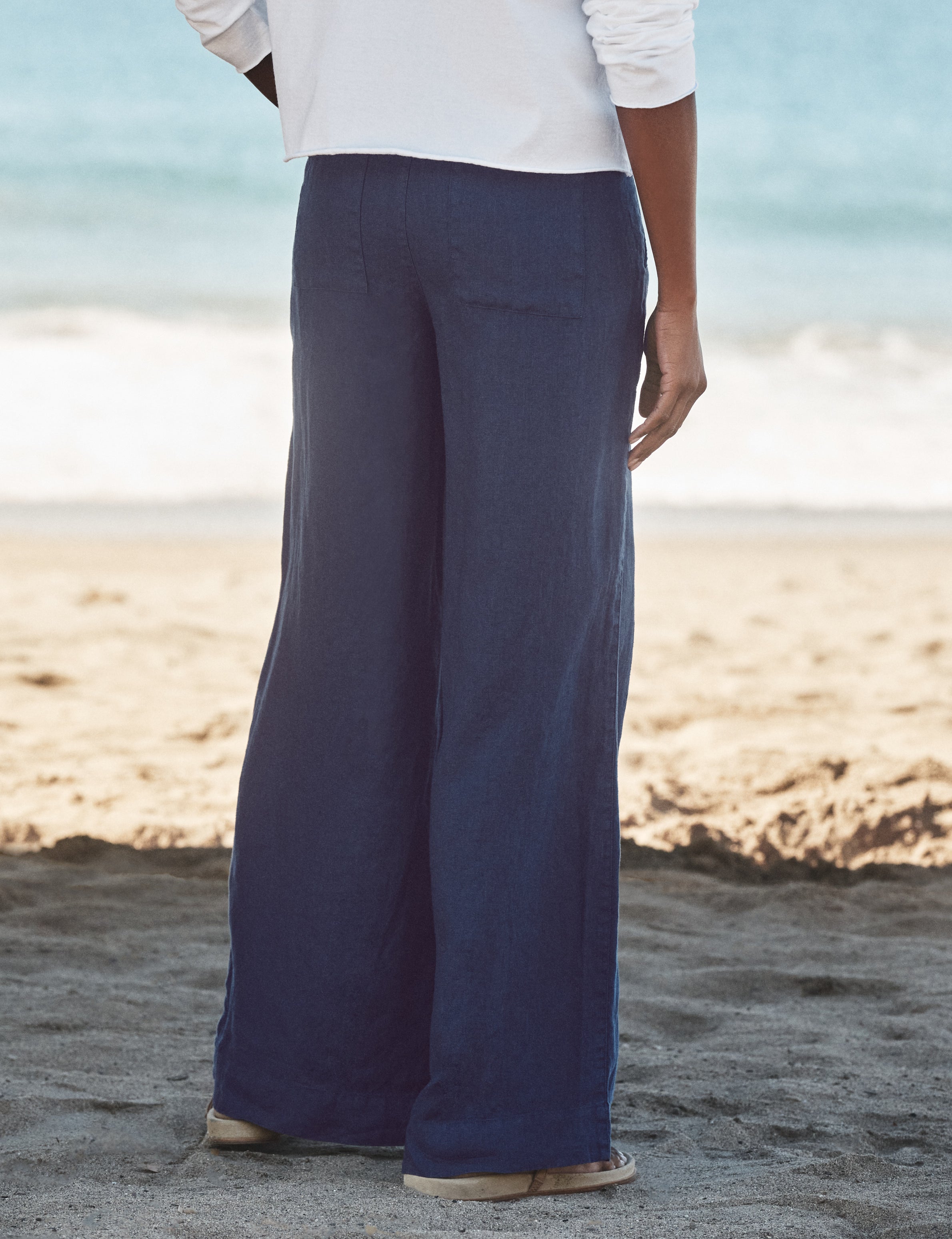 Person wearing navy pants and a white shirt on a beach, alternate view