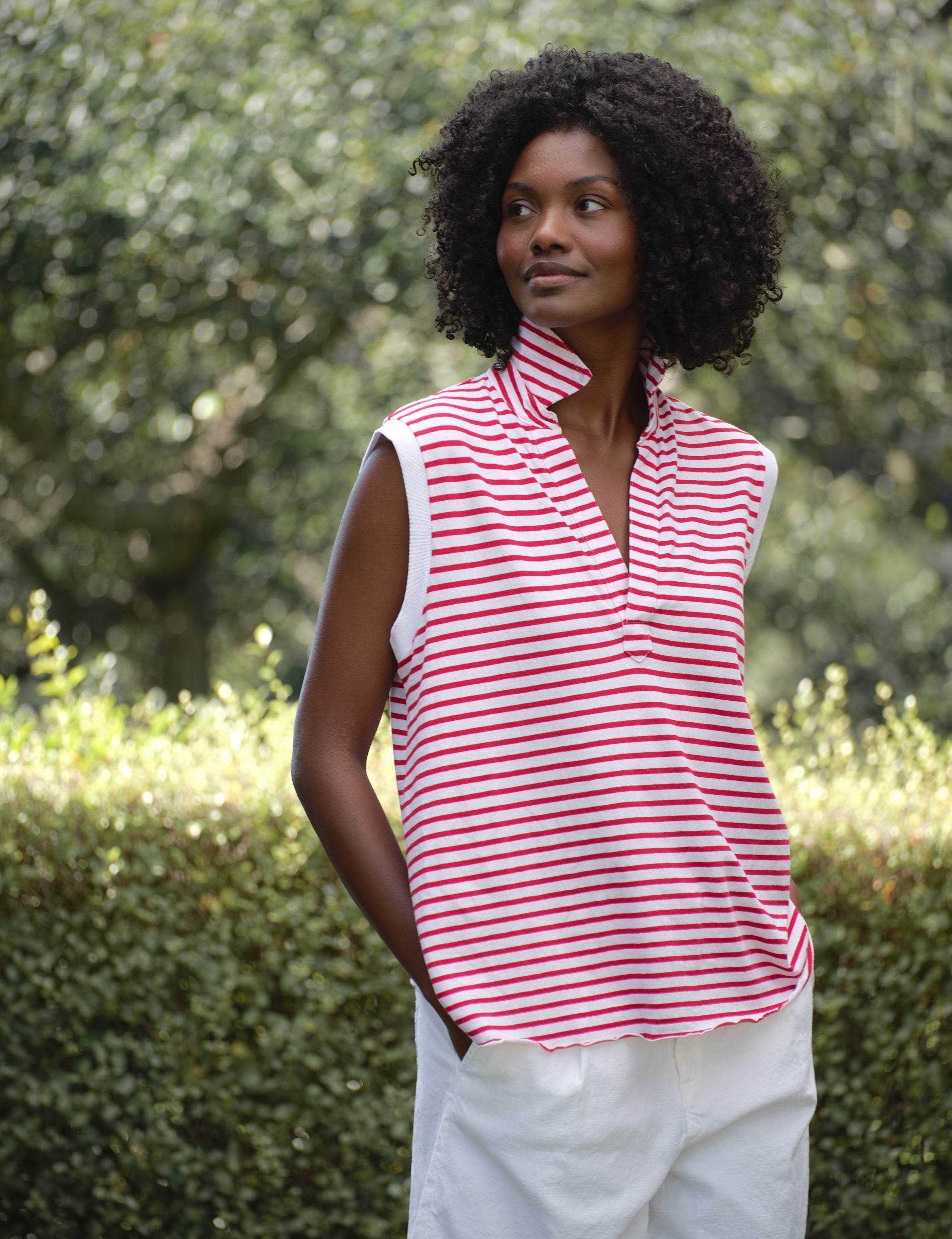 Woman wearing a red and white striped sleeveless top with a blurred green background, front view