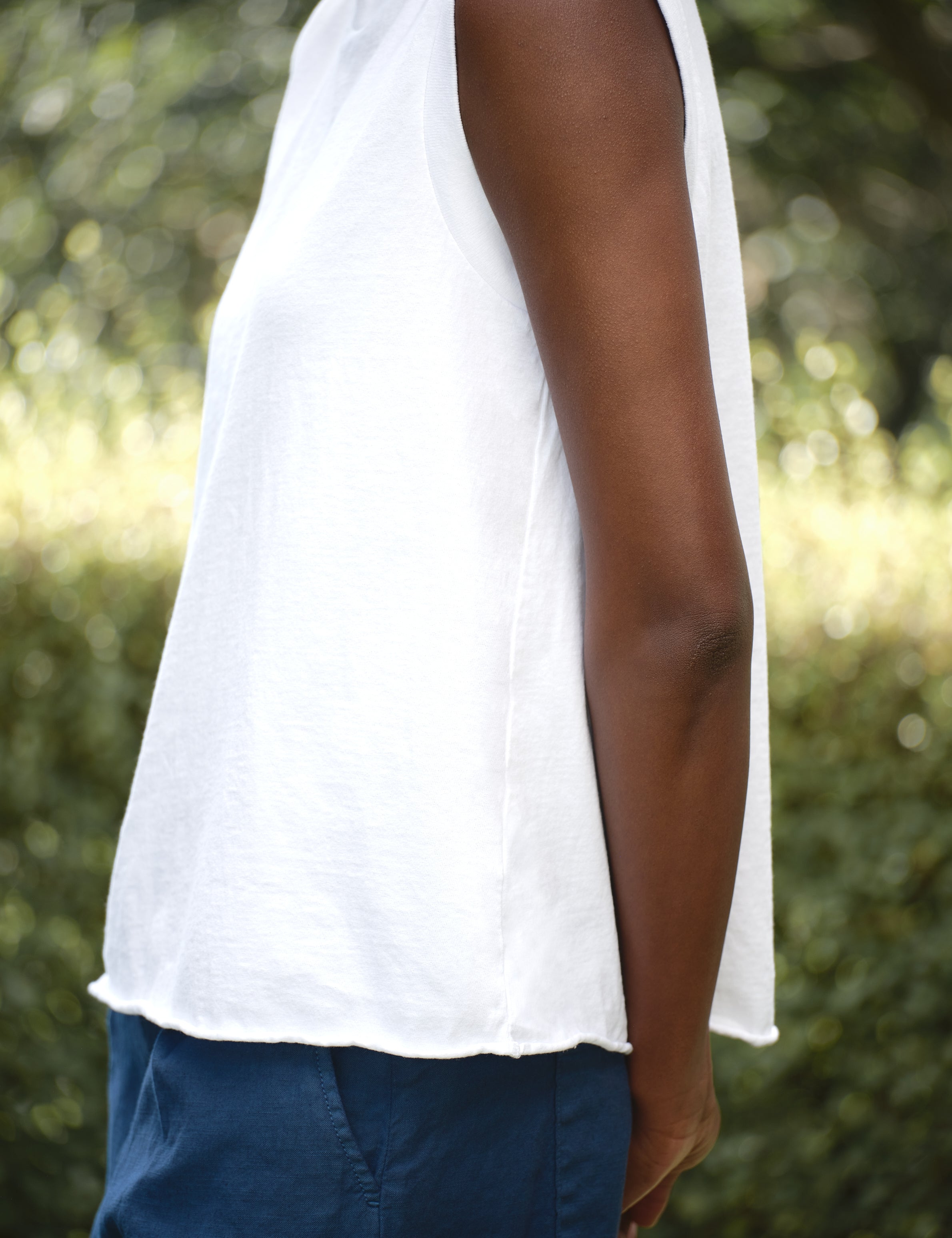 Person wearing a white sleeveless top and blue shorts with a blurred green background, view 5