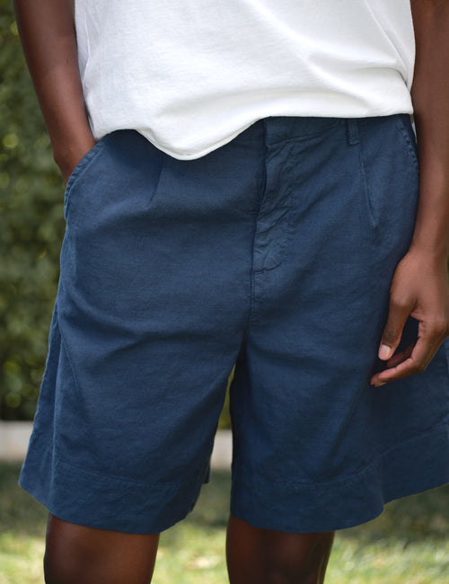 Person wearing blue shorts and a white shirt with a blurred green background, view 3