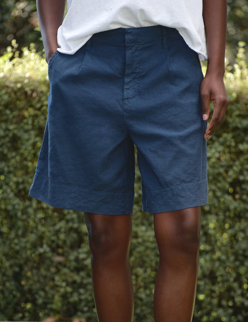 Person wearing blue shorts standing on grass with a blurred green background, front view