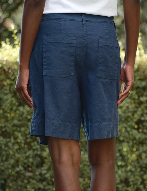 Person wearing blue shorts standing outdoors with greenery in the background, alternate view