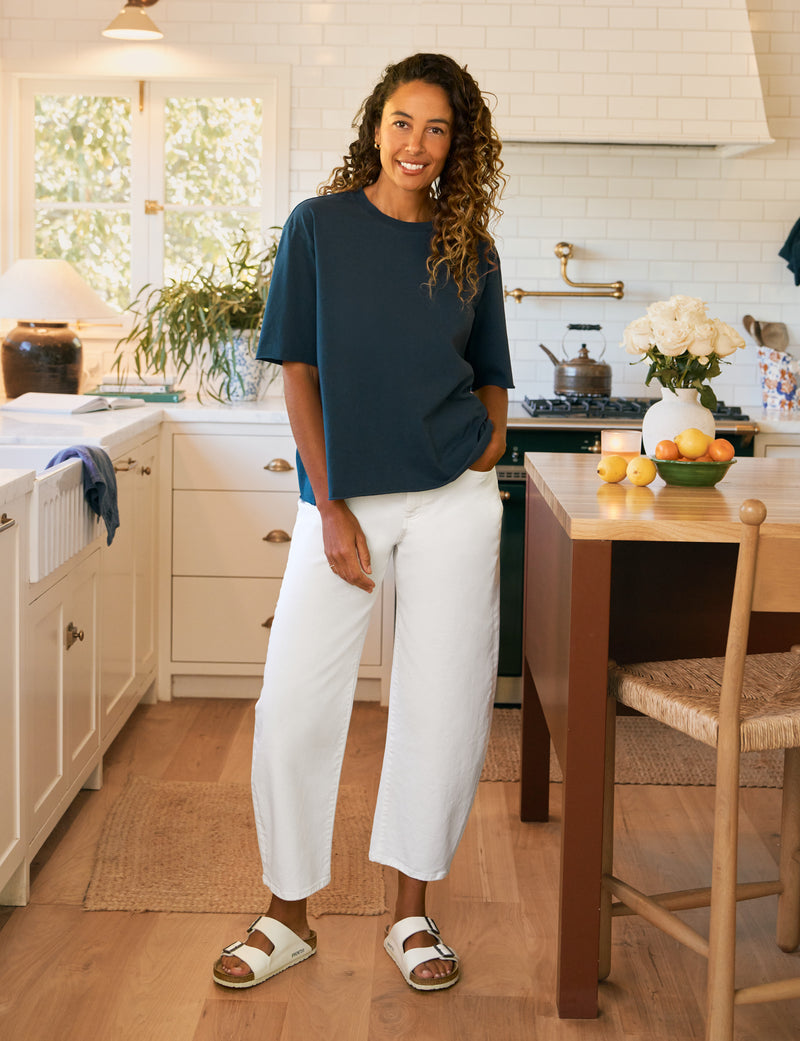 Woman standing in a kitchen wearing a blue shirt and white pants.