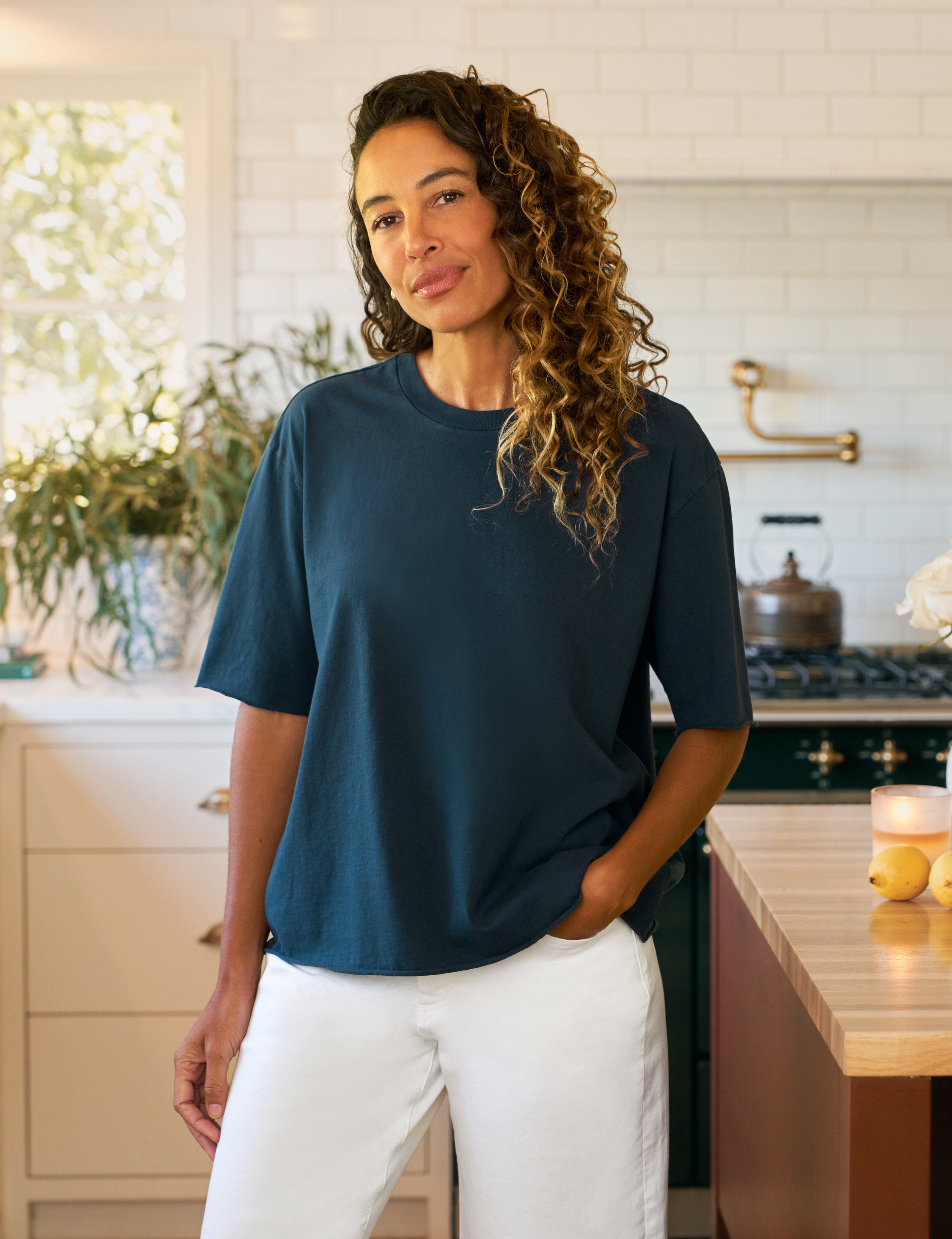 Woman wearing a blue shirt and white pants standing in a kitchen.