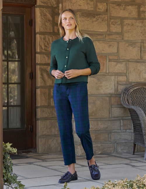 A woman stands on a stone porch wearing a dark green long-sleeve button-front cardigan, dark blue plaid cropped trousers, and dark loafers., view 3