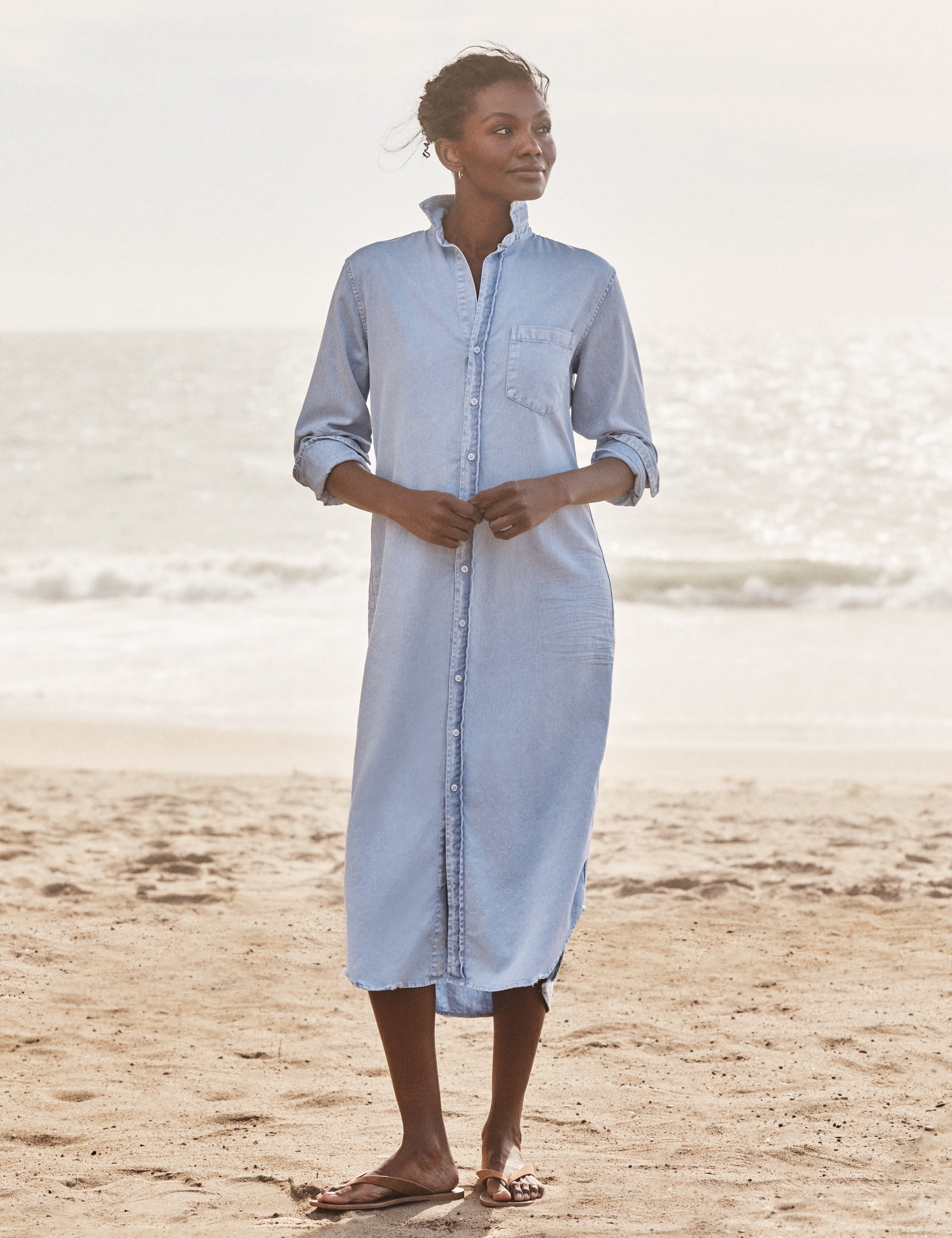 Woman wearing a light blue dress standing on a beach with ocean in the background, front view