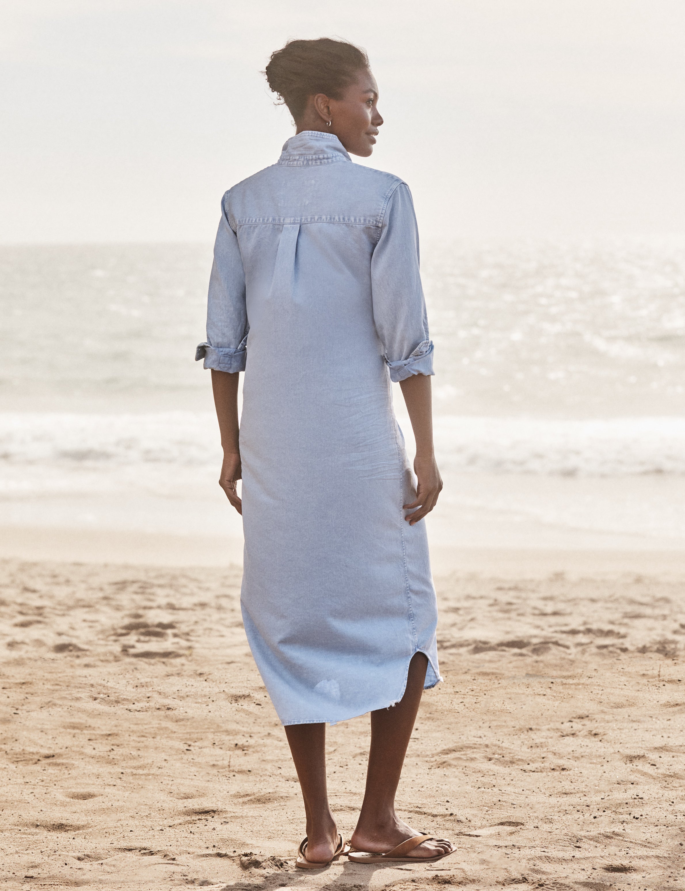 Woman wearing a light blue dress standing on a beach with ocean in the background, alternate view