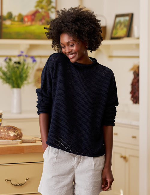 Woman wearing a navy sweater and tan shorts in a kitchen setting, front view