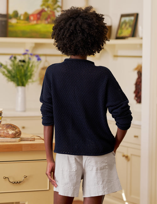 Person wearing a navy sweater and light shorts in a home setting, alternate view