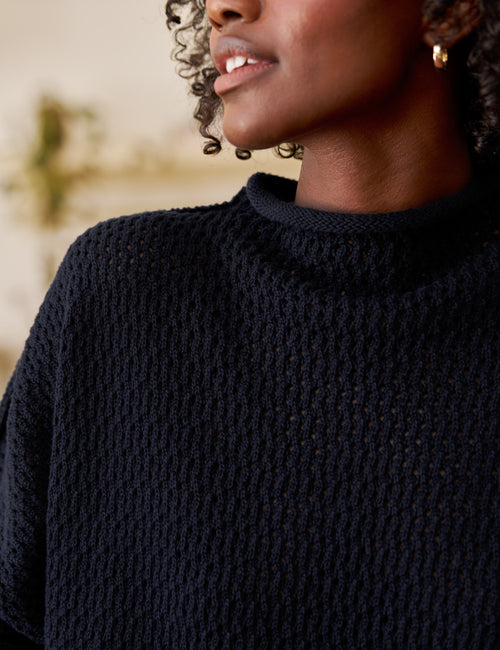 Person wearing a dark blue knitted sweater with a blurred background, view 3