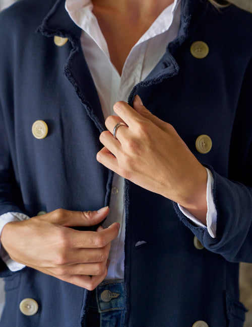 A close-up of a person wearing a navy blue double-breasted jacket with frayed edges and large cream buttons, layered over a white collared shirt., view 3