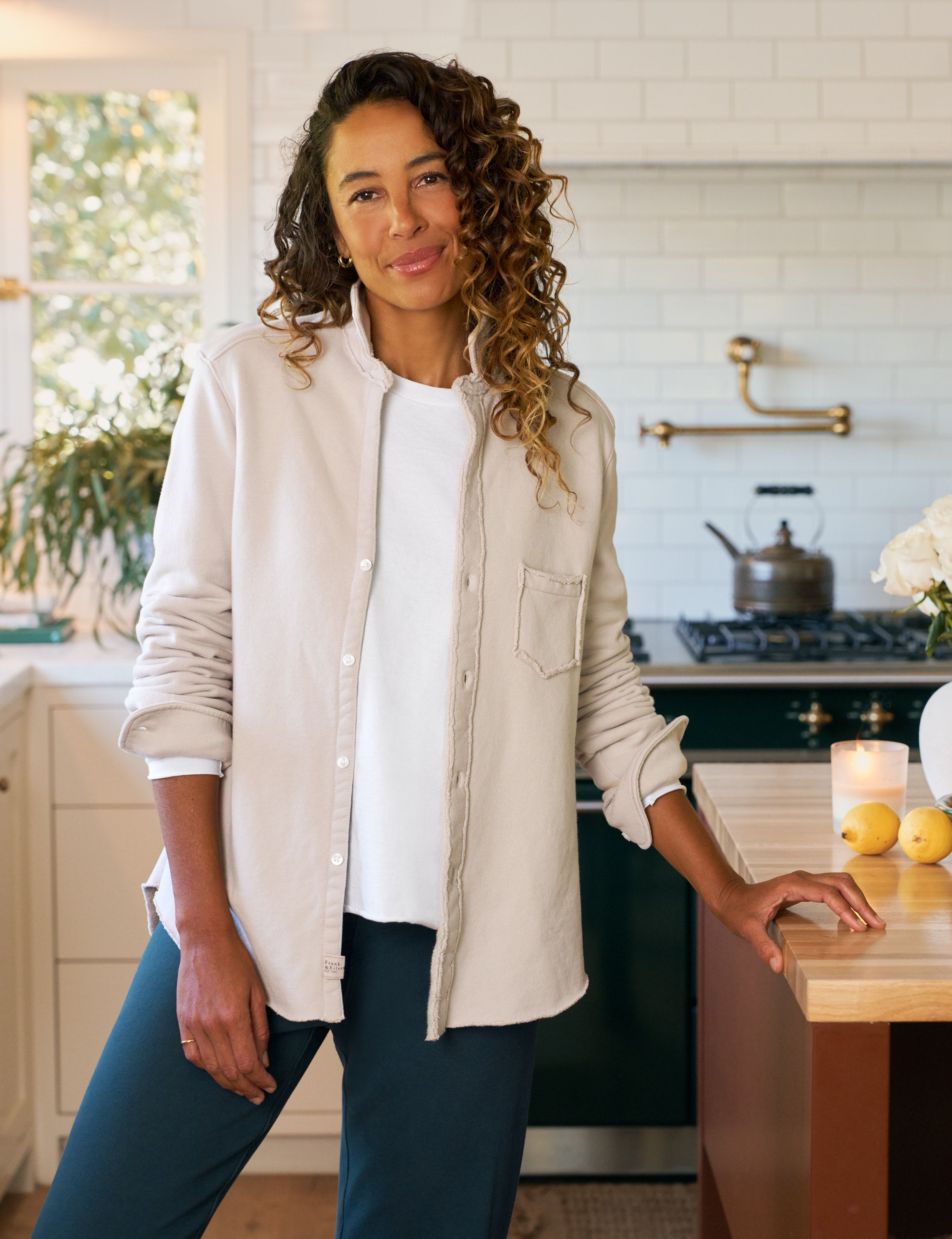 Woman standing in a kitchen wearing a beige jacket and white shirt.