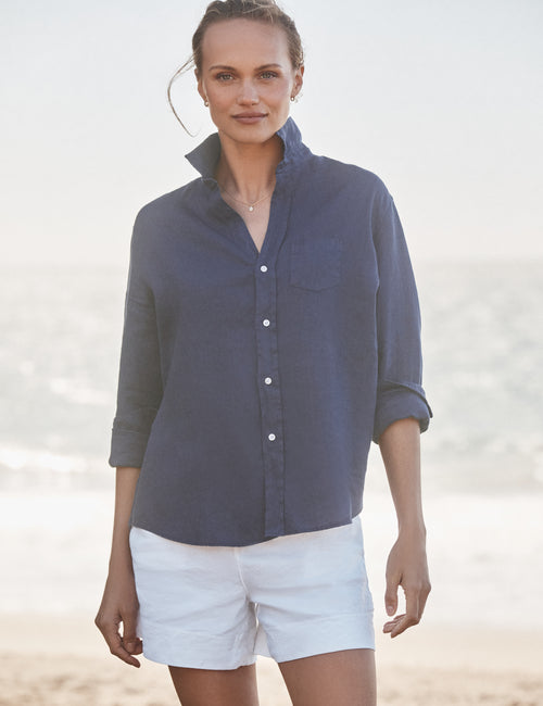 Woman wearing a blue shirt and white shorts on a beach., front view