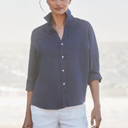 Woman wearing a blue shirt and white shorts on a beach.