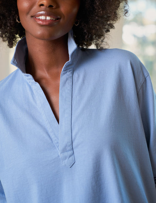 Woman wearing a light blue shirt with a blurred outdoor background, view 3