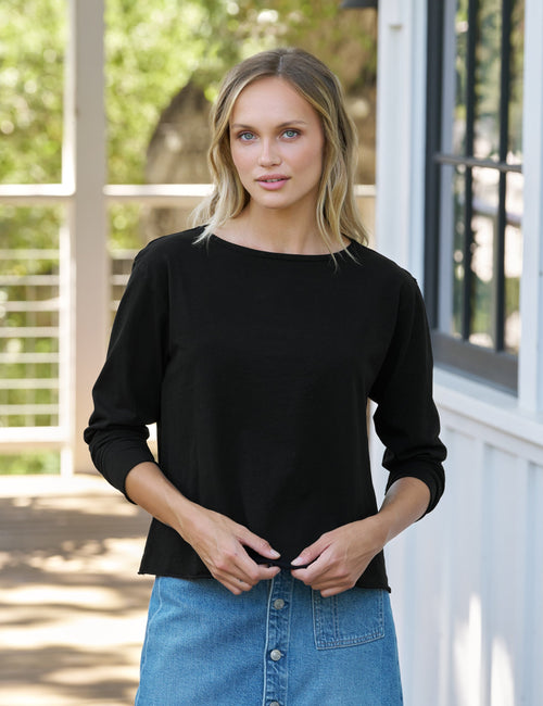 Woman wearing a black top and blue denim skirt standing outdoors., front view