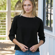 Woman wearing a black top and blue denim skirt standing outdoors.