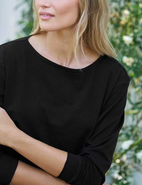 Person wearing a black long-sleeve top with a blurred natural background, view 3
