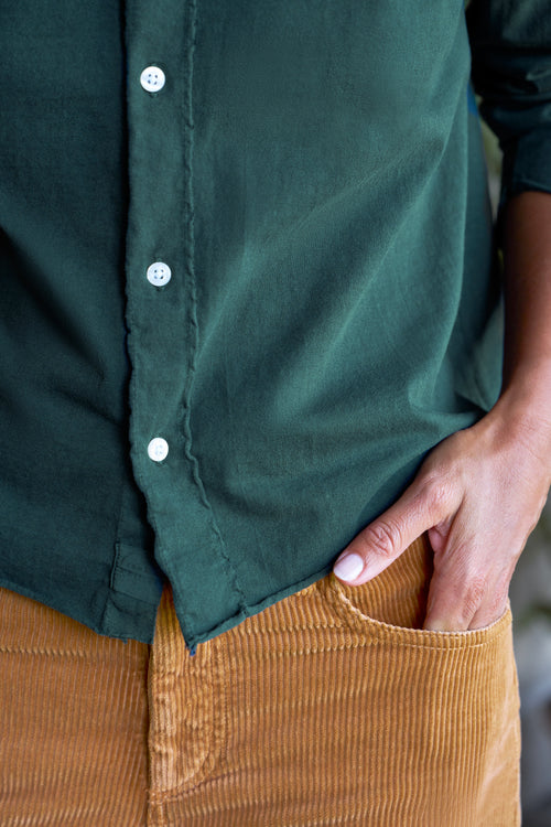 Close-up of a person wearing a dark green button-front shirt tucked into mustard corduroy pants, with one hand in the pocket., view 3