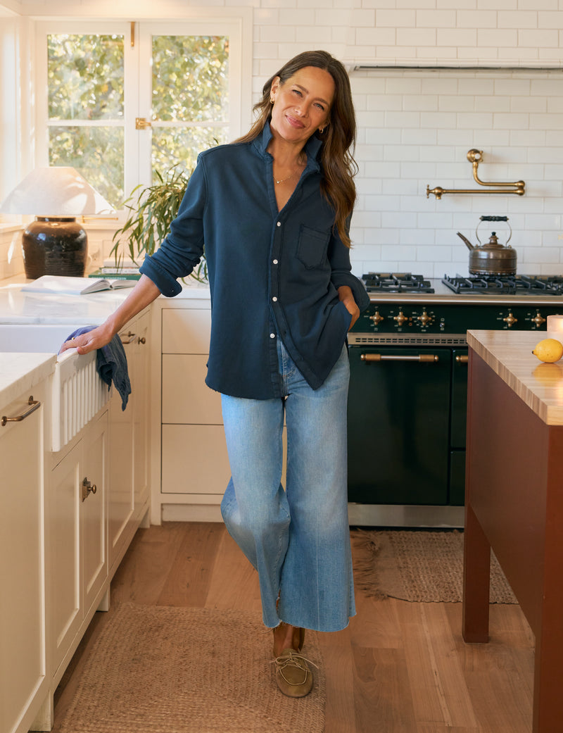 Woman standing in a kitchen wearing a blue shirt and jeans.