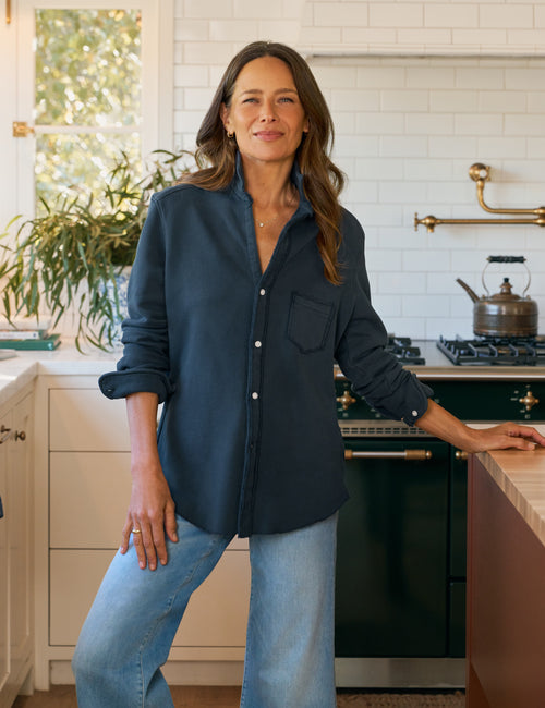 Woman standing in a kitchen wearing a navy shirt and jeans., front view
