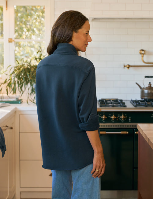 Woman standing in a kitchen wearing a blue shirt and jeans., alternate view