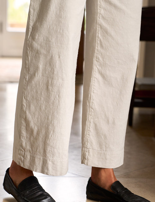 Close-up of a person wearing beige wide-leg linen trousers and black leather loafers, standing in a brightly lit indoor space., view 3