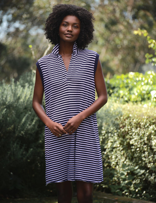 Woman wearing a navy and white striped dress standing outdoors with greenery in the background, view 5