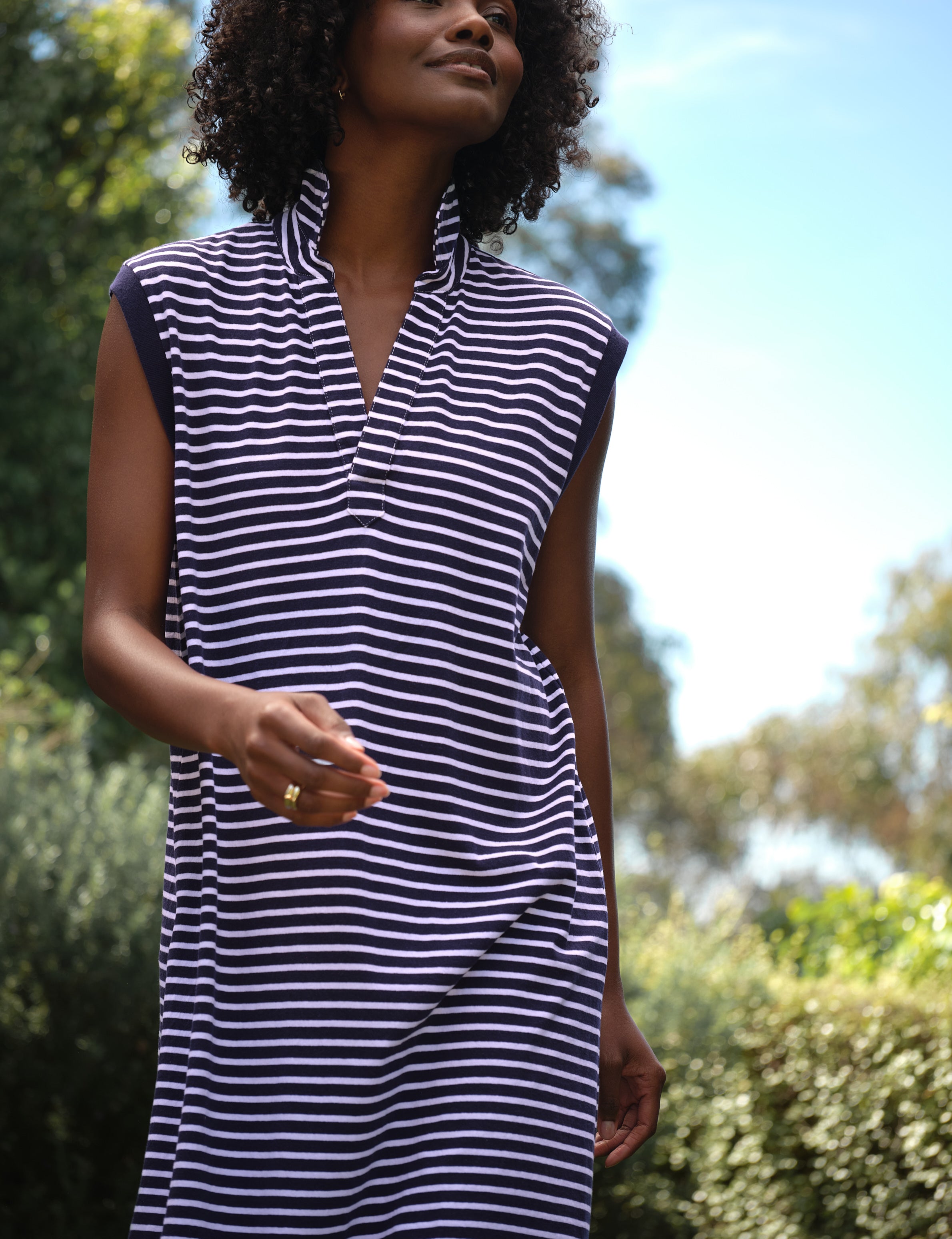 Woman wearing a navy and white striped dress outdoors with greenery in the background, view 4