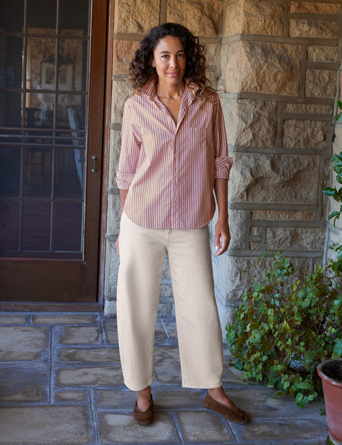 A woman stands on a stone porch wearing a orange and white vertically striped button-down shirt with rolled sleeves, beige wide-leg cropped pants, and brown flats., view 4