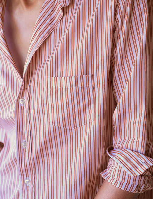Close-up of a person wearing a long-sleeve button-up shirt with vertical orange and white stripes, featuring a chest pocket and rolled sleeves., view 3