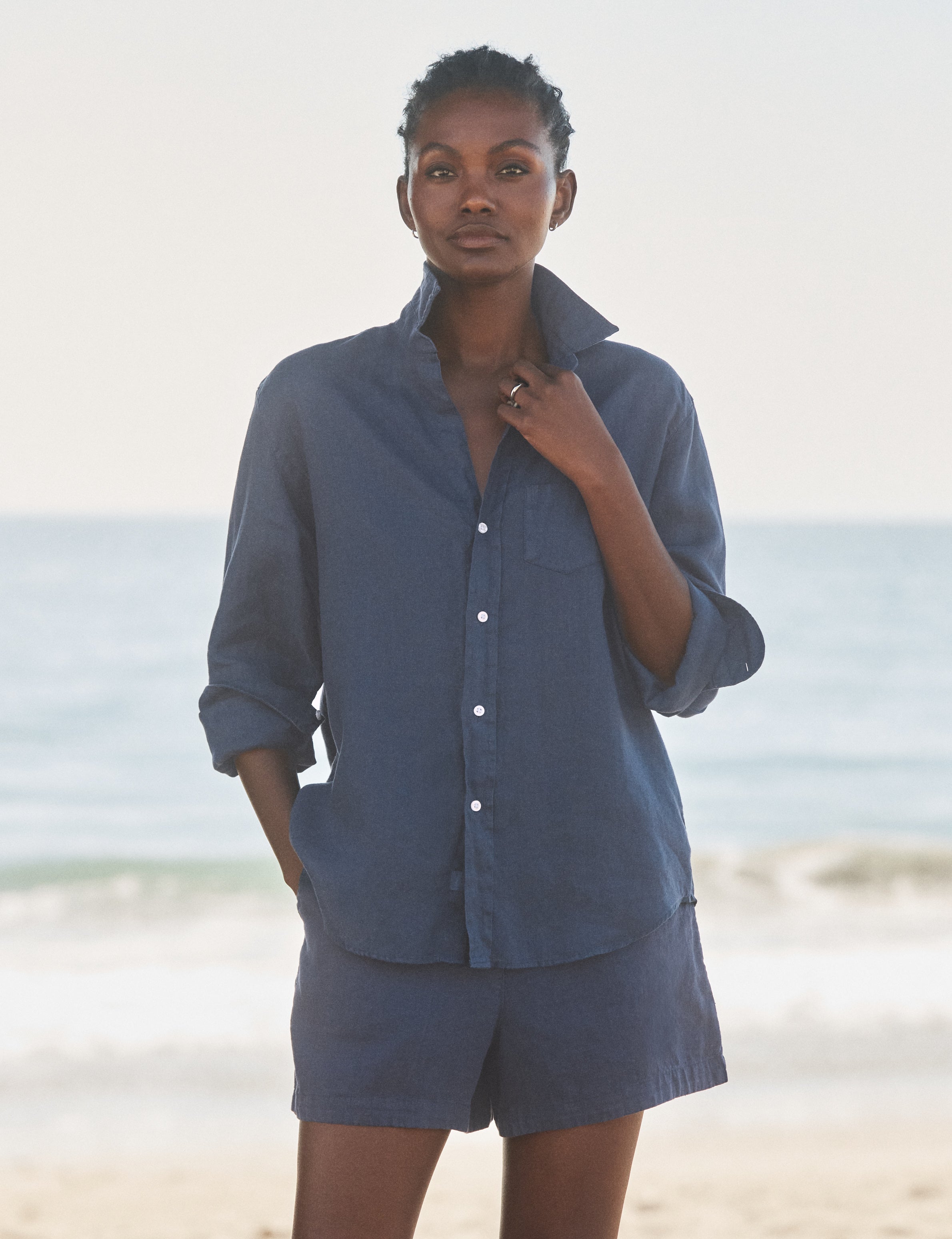 Woman wearing a blue shirt and shorts standing on a beach., view 3