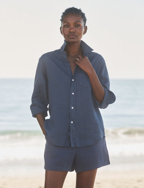 Woman wearing a blue shirt and shorts standing on a beach., view 3