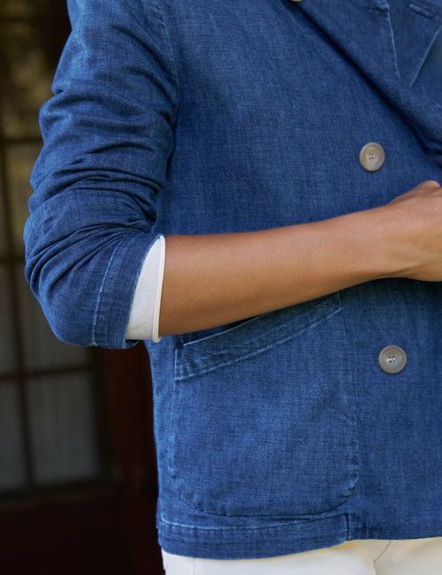 Close-up of a person wearing a blue denim-style blazer or jacket with rolled sleeves and visible white shirt cuffs underneath, against an indoor background., view 4