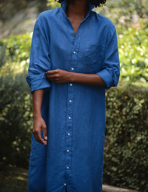 Person wearing a blue dress with a blurred green background, view 3