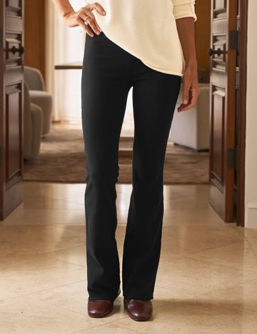 Person wearing black pants and a cream top in a room with wooden flooring and furniture.