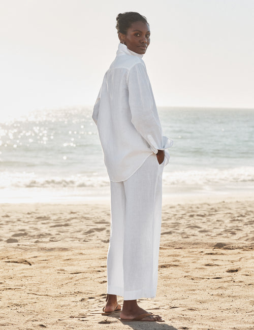 Person wearing a white outfit standing on a beach with ocean in the background, alternate view